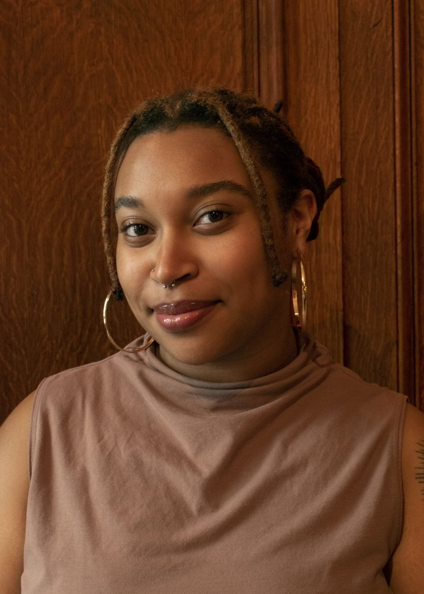 headshot of a young person in a light brown top and gold earrings.